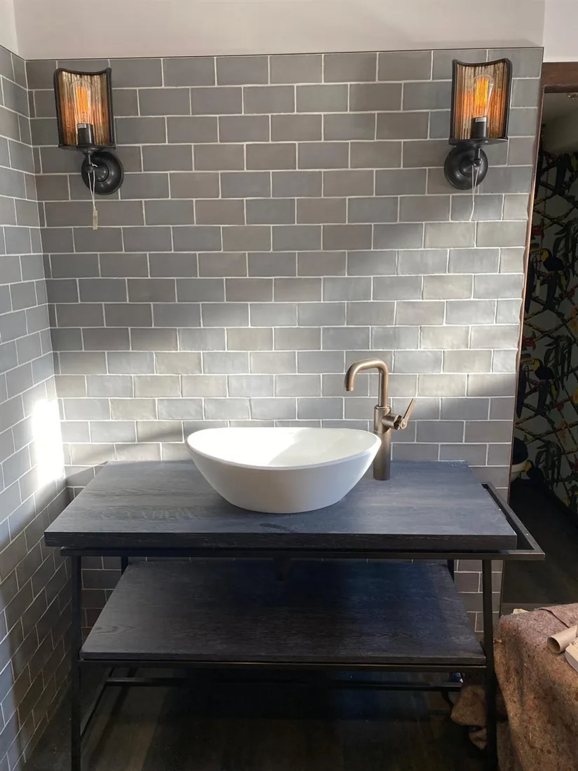 Grey brick-tiled bathroom with vessel basin, dark timber vanity and copper wall lights