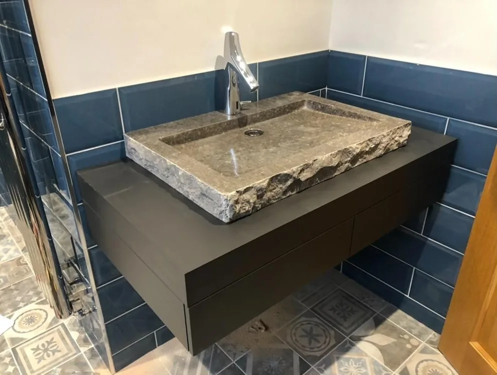 Carved natural stone basin on a floating vanity with navy tiled splashback